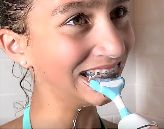 Young girl with braces is water flossing with a seven stream  water flosser gum massager around her braces, in the shower.
