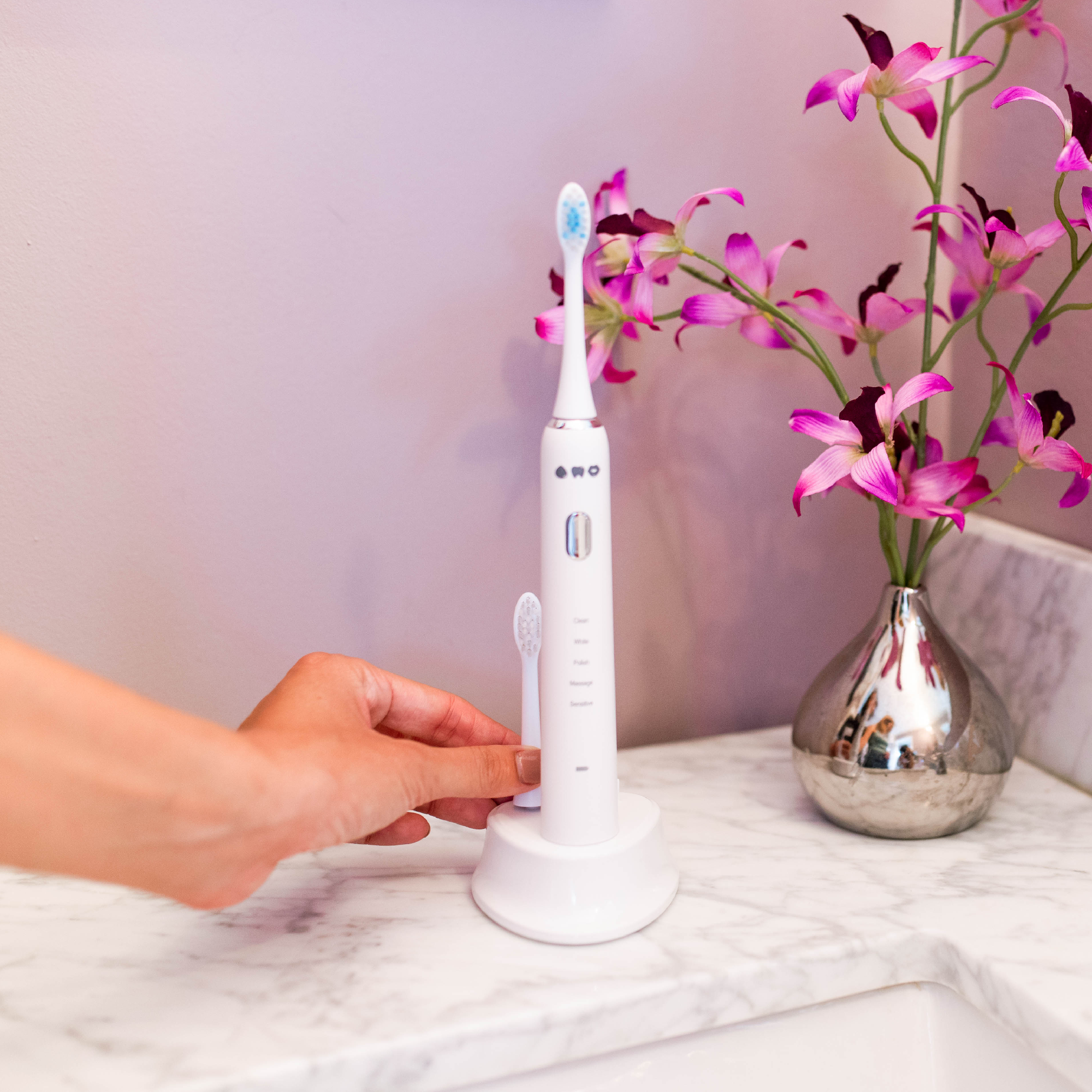 pretty sonic toothbrush on charging next to sink with a girls hands 